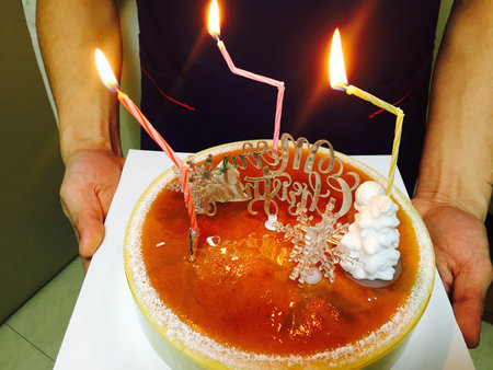 Birthday cake with burning candles in the hands of a man.の写真素材