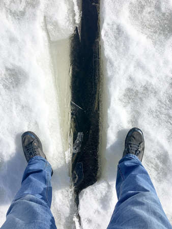 Men's feet over a crack in the ice of the frozen Gulf of Finland. Winter season, Russiaの写真素材