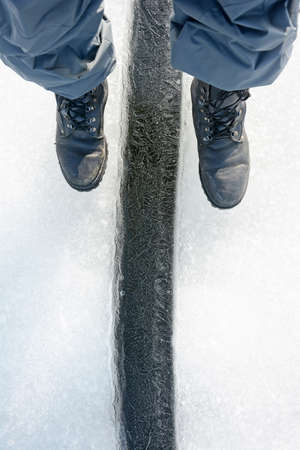 Men's feet over a crack in the ice of the frozen Gulf of Finland. Winter season, Russia