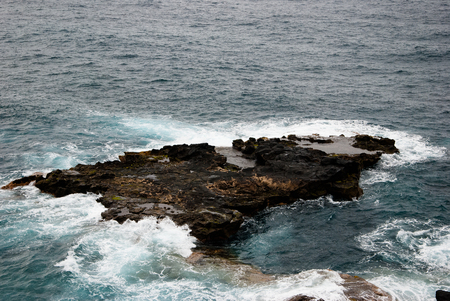 A dark rock in the waves of the oceanの写真素材