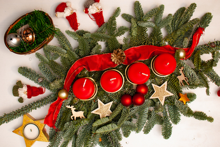 An advent wreath with four red candles on a fir branch surrounded by Christmas decoration on a white tableの写真素材
