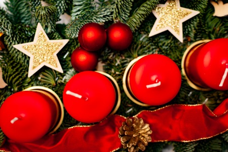 An advent wreath with four red candles on a fir branch surrounded by Christmas decoration on a white tableの写真素材