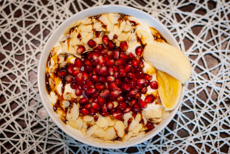 A white bowl filled with muesli, oats, pomegranate, banana, seeds, oat milk and maple syrupの写真素材