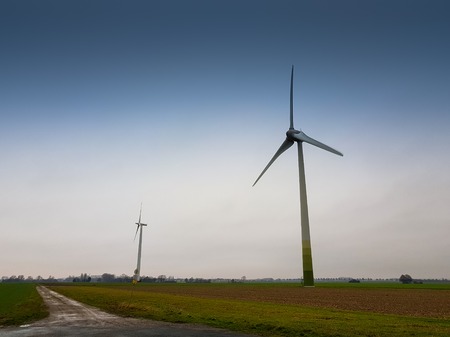 A bike lane, a green field and wind mills in the back before the blue skyの写真素材