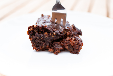 Side view of vegan chocolate brownie with nuts and a fork white plateの写真素材