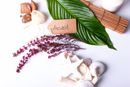 A set up of wellness items, a bamboo mat, a shell, candles, a branch, wood, a starfish and a sign saying "'Time off" in Germanの写真素材