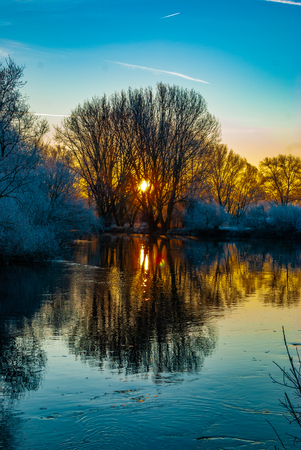 The frozen world in the early morning during colorful sunrise near a river in winterの写真素材