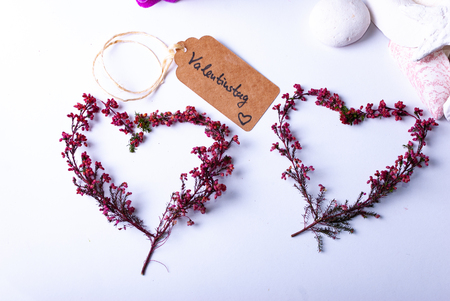 A label saying "Valentinstag" and colorful red branches, stones, candles, orchids and a bamboo mat and a palm leaf on white background with copy space and two heartsの写真素材