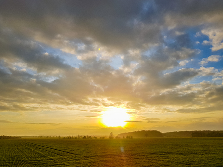 Panorama of a sunset on the cloudy sky over a green field, mountains in the backの写真素材