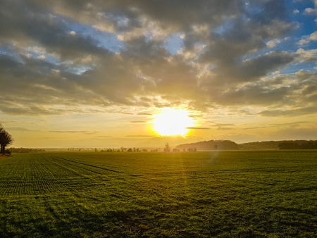 Panorama of a sunset on the cloudy sky over a green field, mountains in the backの写真素材