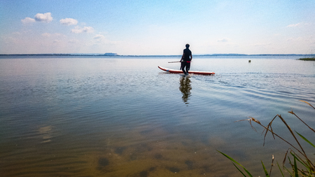 A big empty lake with a silhouette of an single sportsman doing stand up paddlingの写真素材