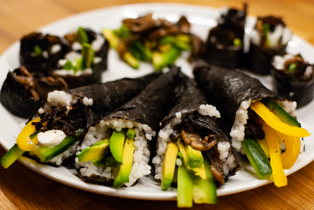 Side view homemade vegan Sushi rolls and temaki filled with avocado on a plate on a wooden tableの写真素材