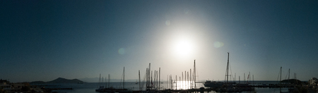Silhouettes of sail boats in the ocean, the blue sky and the sun in the background - back lightの写真素材