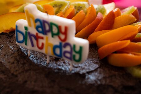 A home made vegan chocolate cake with fresh fruit and a candle saying Happy Birthday - close up