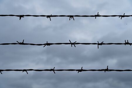 Three rows of barbed wire in front of the dark and cloudy sky - security concept