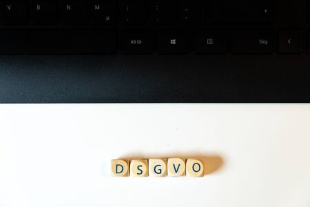 Wooden cubes with the German word DSGVO for GDPR together with a black keyboard on white background...