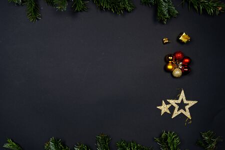 Christmas ornaments (Christmas baubles, stars and little presents) on black background framed by fir twigsの写真素材