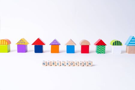 Cubes with letters saying "Nebenkosten", the German word for additional costs in front of a row of houses built of toy colorful toy blocksの写真素材