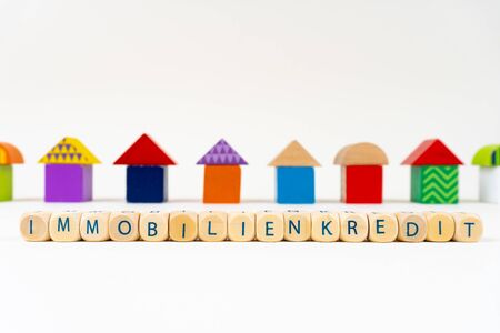 Wooden block with letters saying "Immobilienkredit" (German for real estate loan) in front of colorful toy housesの写真素材