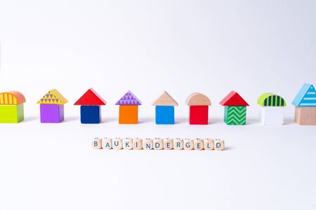 Cubes with letters saying "Baukindergeld", the German word for money for building a house for families in front of a row of houses built of toy colorful toy blocksの写真素材