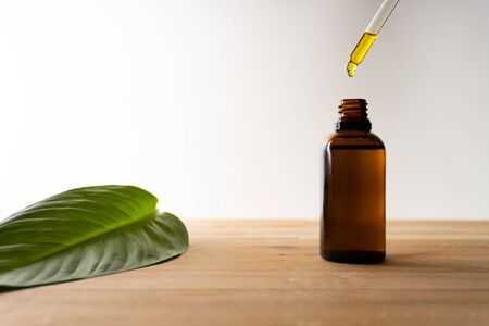 CBD oil or any other oil dropping into a small bottle standing on a wooden board - white background
