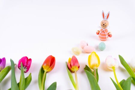Colorful tulips laying in a row with easter eggs and a easter bunny on white background with copy spaceの写真素材