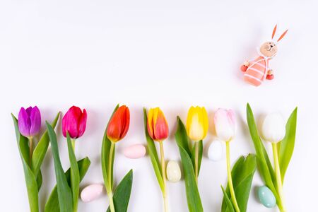 Colorful tulips laying in a row with easter eggs and a easter bunny on white background with copy spaceの写真素材