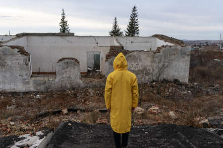 a man in a yellow protective cloak stands among the destroyed building. place after a man-made...