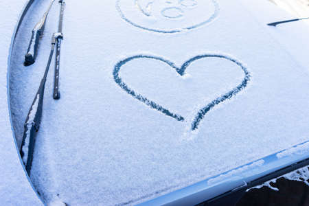 Heart love symbol on windscreen of car in snow. View of a snow car after a snowfall