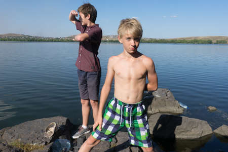 boys standing on the shore of the lake. two friends near the lake. boy stands near a lake in swimming shorts. Boy sunbathing.の写真素材