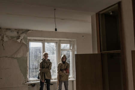 boys standing in an abandoned building. wandering boy. man in a protective cloak with a hood. Post apocalypse. traveling on foot in a post-apocalyptic world. teenagers with machetesの写真素材