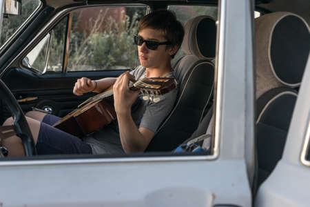 Two young man in the car. boy plays the guitar in the car. cheerful company of young people. journey together. fun pastime.の写真素材