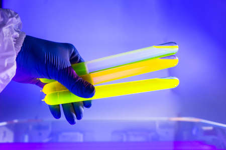 Fluorescein glowing in flask under ultraviolet light. A closeup of man hand holding up a vial fluorescent liquid.の写真素材