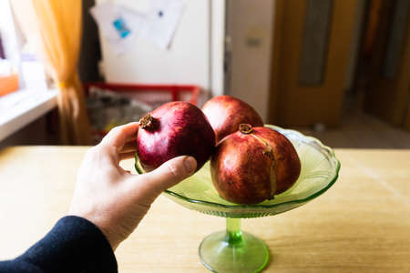 holding a pomegranaten in his hand. basket full of a pomegranates on the kitchen table.の写真素材