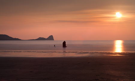 Sunset at Rhossili Bay and Worms Head showing remains of the ship The Helvetia, a Norwegian barque, which was wrecked during a storm in 1887 on the Gower peninsula, South Walesの写真素材