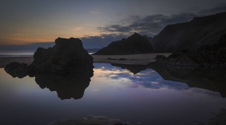 Rockpools and reflections at sunset on Three Cliffs bay on the Gower peninsula, Swansea, Wales, UK