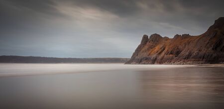 Low tide at the magnificent rocky outcrop called The Great Tor on Three Cliffs Bay, Gower, Swansea, UKの写真素材