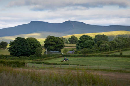 Editorial Brecon, UK - July 04, 2022: A tractor under the twin peaks of Penyfan and Corn Du in the Brecon Beacons National Park in South Wales UKの写真素材