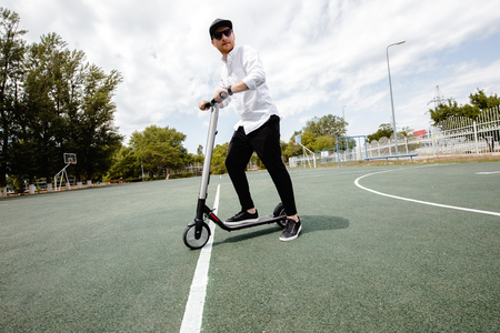 Modern man in stylish black and white outfit riding electric scooter in the cityの写真素材