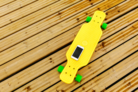The phone lies on a yellow plastic longboard, which is located on the wooden flooring. Top view