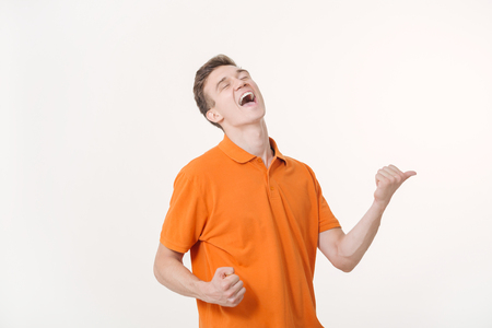 Emotional young man with brown hair screaming and showing thumbs up, feeling excited. Success conceptの写真素材