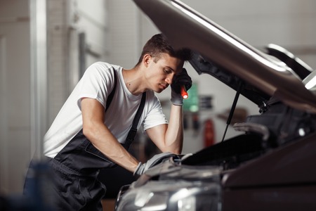 A young mechanic is puzzled while working at a car service and m