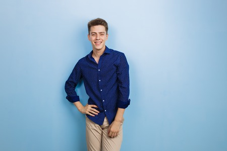 Handsome friendly looking cheerful european guy wearing blue shirt smiling standing over blue wallの写真素材