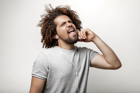 A curly-headed handsome man wearing a gray T-shirt is listening to music in the earphones with an...