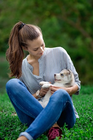 A beautiful woman with a ponytail and wearing a striped shirt is holding a sweet husky puppy on the lawn. Love and care for pets.の写真素材