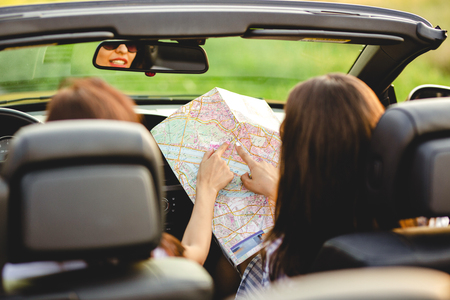 Two dark-haired women are sitting a black cabriolet and exploring the map.の写真素材