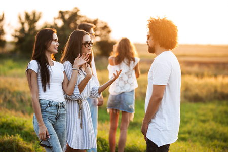 Two young dark-haired women chatting with young curly man outdoor on a warm day.の写真素材