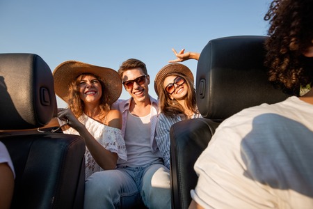 Charming young dark-haired women in hats are sitting with young  man in a black cabriolet and smiling on a summer day.の写真素材