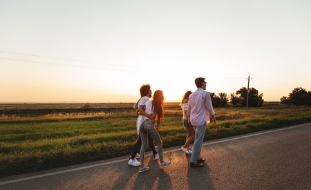 Company of happy young stylish guys walk along the road. on a sunny dayの写真素材