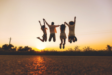 Company of young girls and guys are jumping in the field on a summer day and holding their hands up at sunsetの写真素材
